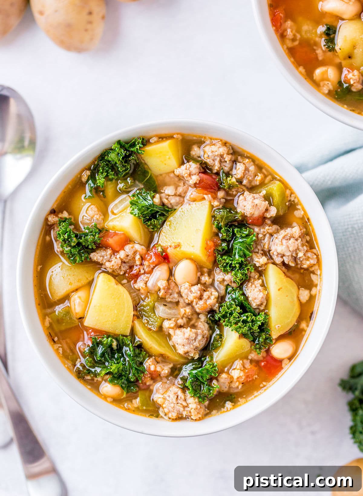 A beautiful, vibrant bowl of Sausage Kale Soup viewed from above, with two spoons invitingly placed on the side, ready to be enjoyed.