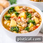 A pristine bowl of Sausage Kale Soup, presented elegantly on a white surface with a spoon to the side, highlighting the dish's warmth and homemade appeal.