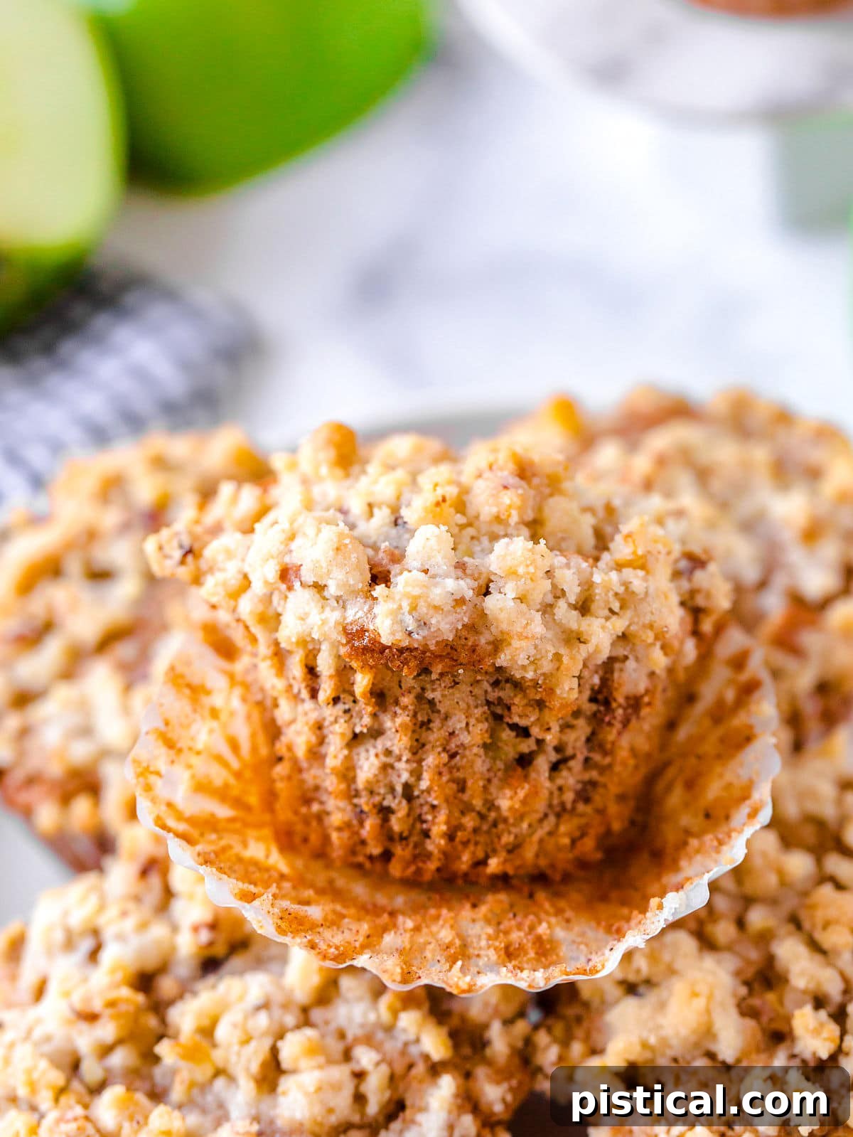 apple muffin unwrapped sitting on a plate of muffins