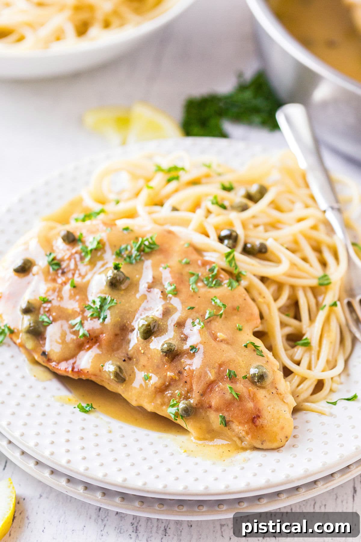 chicken piccata plated with pasta on a white plate and topped with fresh parsley.