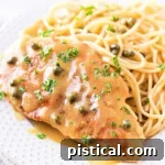easy chicken piccata recipe plated on a white plate with spaghetti and garnished with parsley.