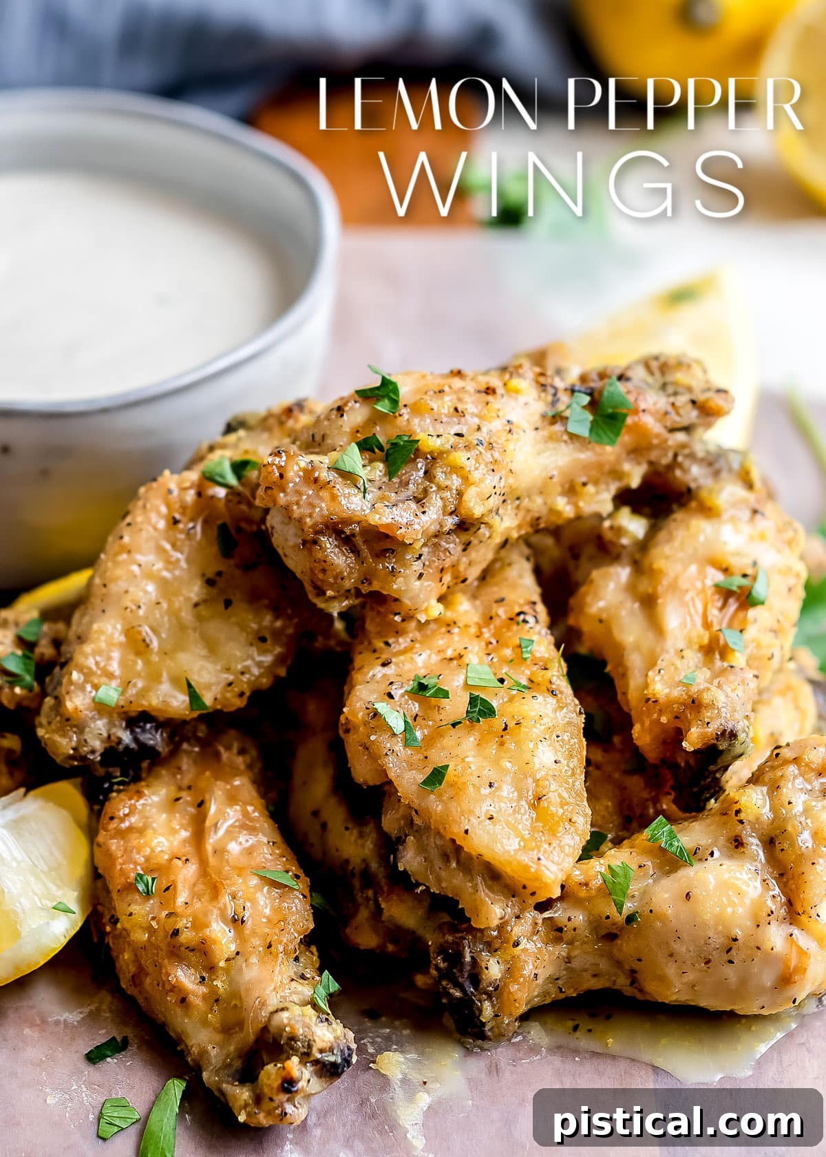 lemon pepper wings stacked in a pile with a bowl of ranch behind them and title overlay at the top