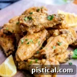 lemon pepper wings stacked in a pile garnished with parsley and lemon wedges sitting on parchment paper