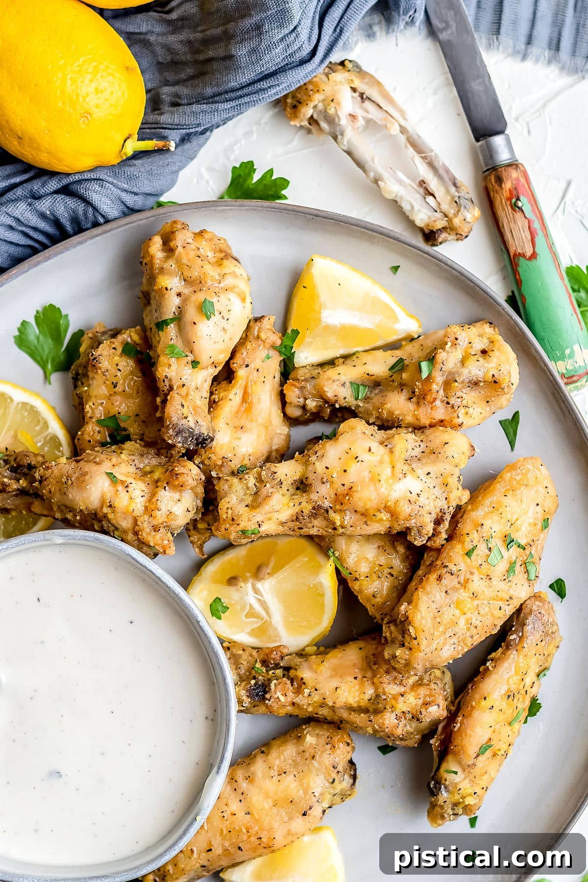 baked chicken wings on plate with ranch in small bowl and garnished with parsley and lemon top down view