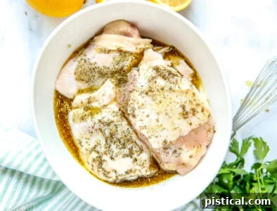 Greek chicken recipe with marinade poured over chicken thighs in a white bowl, ready for baking.