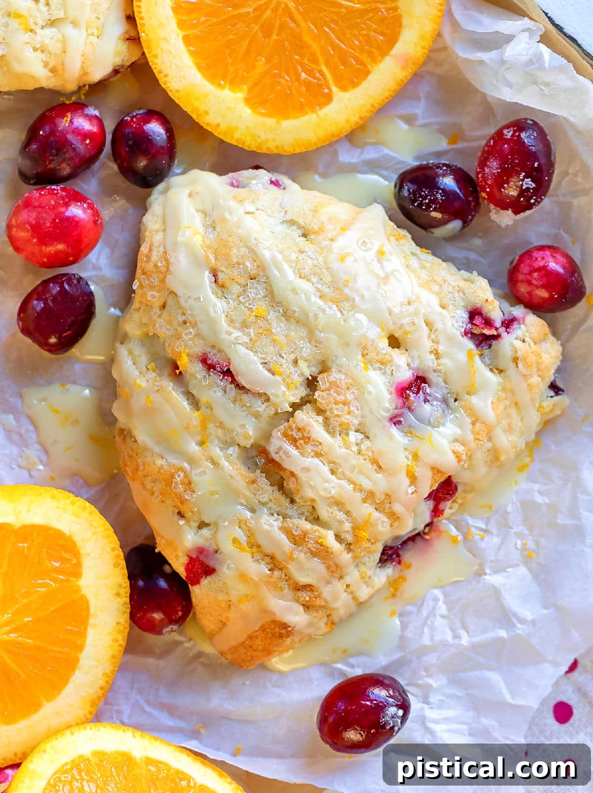 Top-down view of a golden-brown cranberry orange scone, garnished with fresh cranberries and orange slices on parchment paper
