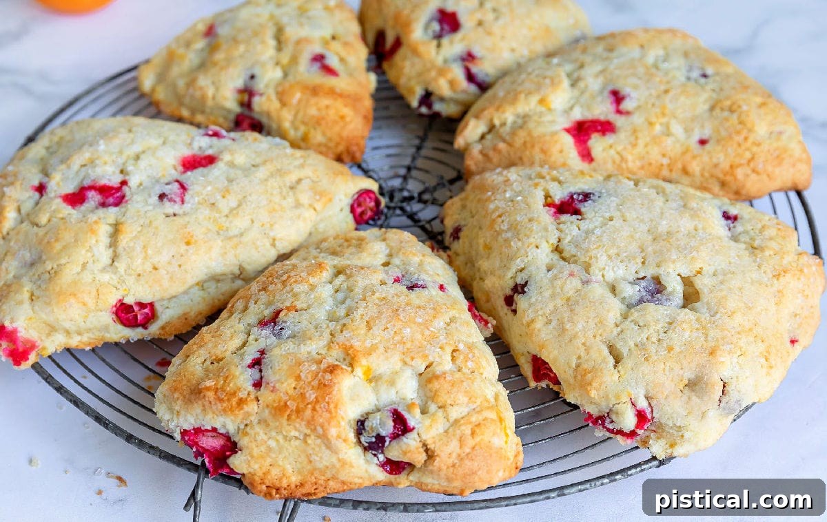 Six baked cranberry orange scones cooling on a wire rack, glistening slightly