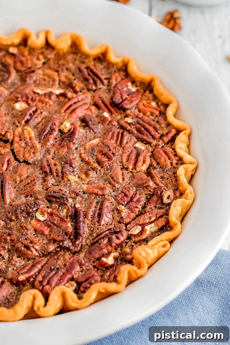 A whole maple pecan pie in a rustic pie plate, resting on a light blue napkin, ready to be sliced and served.