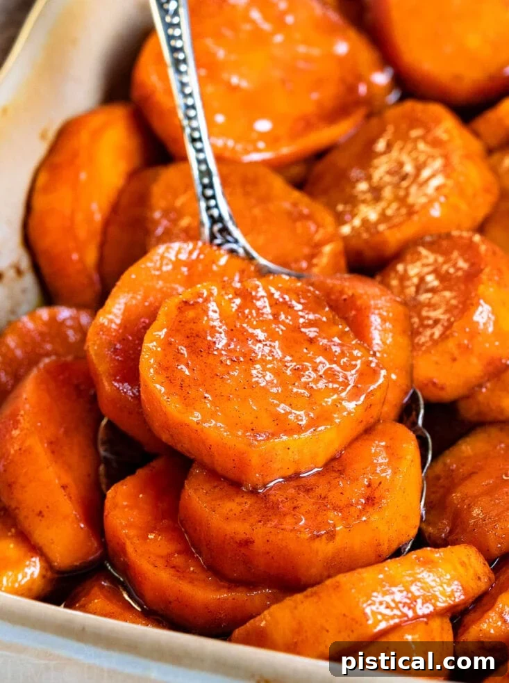 Spoonful of candied sweet potatoes being lifted from a beige baking dish