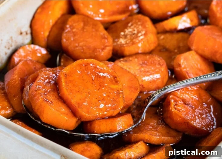 Spoonful of candied sweet potatoes in a beige baking dish, showcasing the texture and glaze