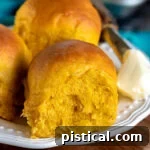 three pumpkin dinner rolls on a white plate with butter on the side