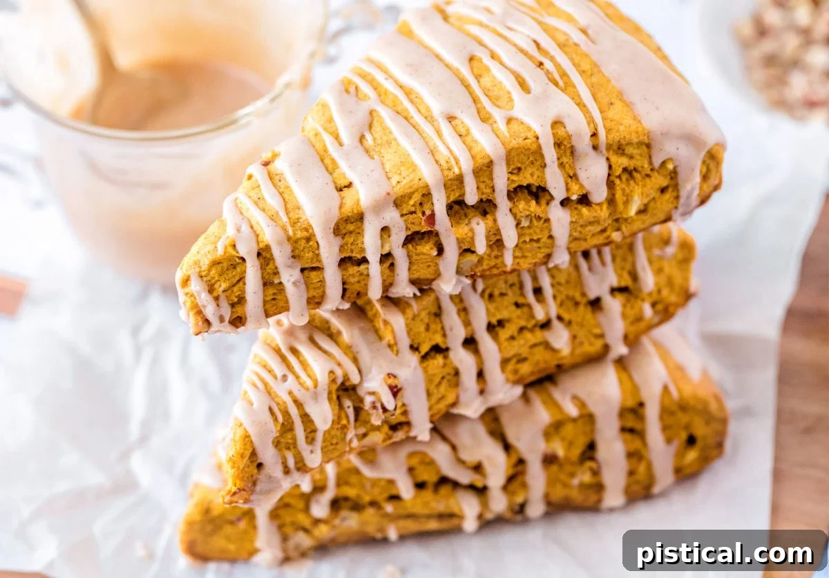 Autumn Spiced Pumpkin Scones with Maple Drizzle 3 stacked pumpkin scones with a generous drizzle of maple glaze on a white backdrop