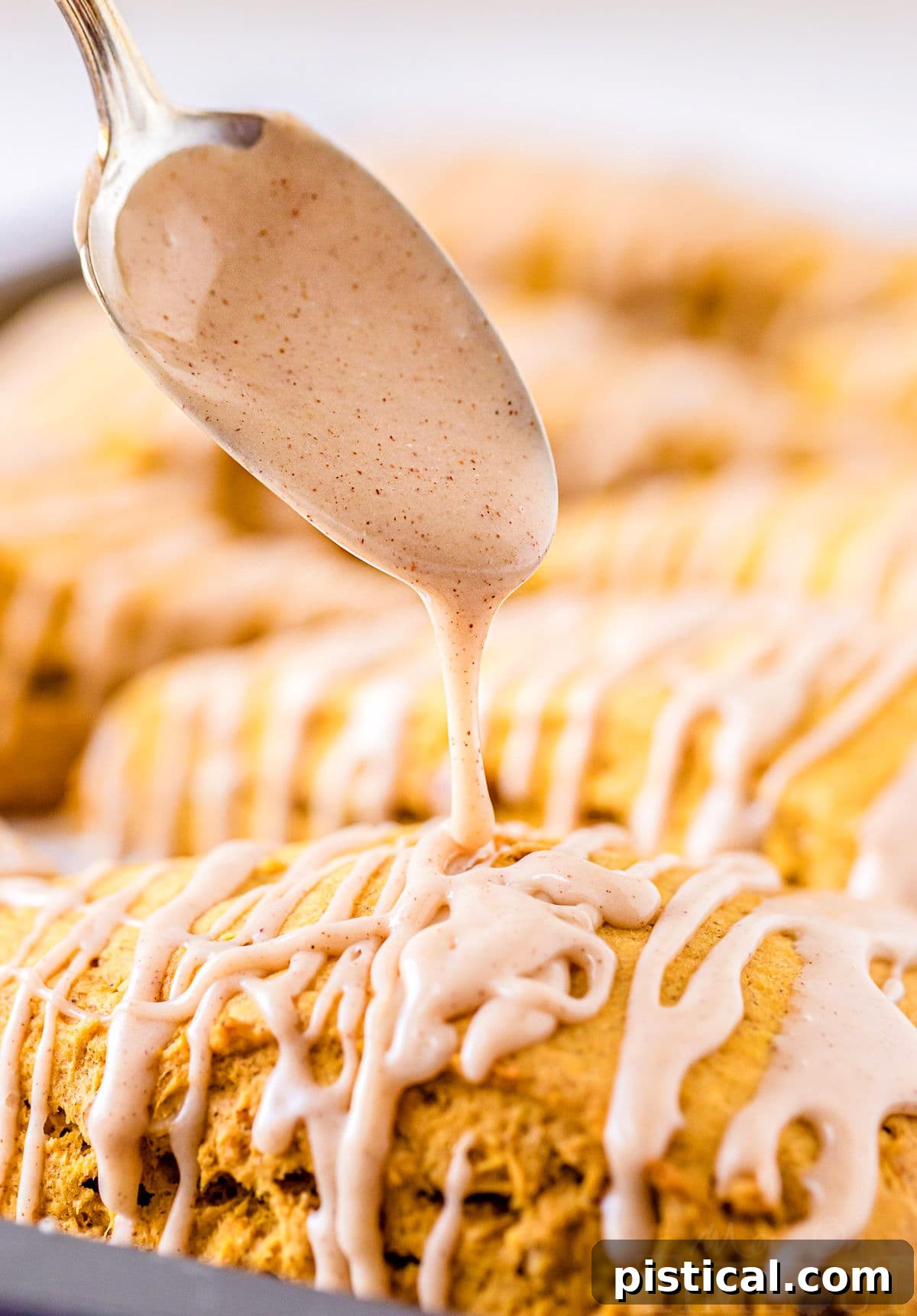 Autumn Spiced Pumpkin Scones with Maple Drizzle 5 maple cinnamon glaze being drizzled over freshly baked pumpkin scones on a baking sheet