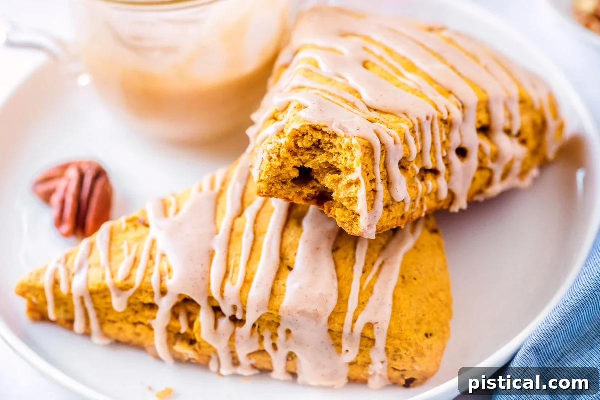 Autumn Spiced Pumpkin Scones with Maple Drizzle 9 pumpkin scone with a bite taken, resting on a white plate next to a blue napkin