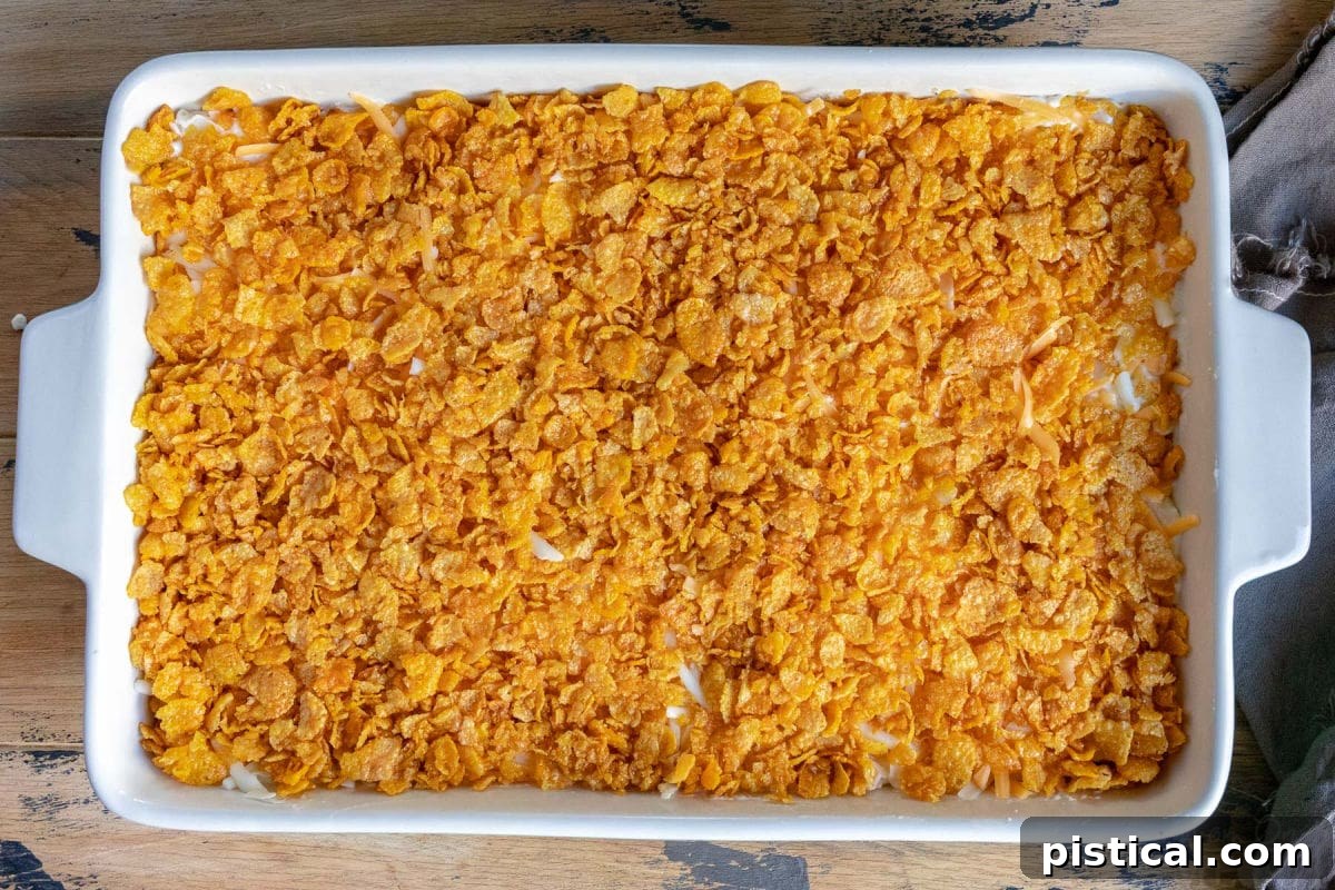 Homestyle Cheesy Potato Casserole 7 A top-down view of the cheesy potato casserole in a baking dish, perfectly topped with a golden cornflake mixture, ready for the oven.