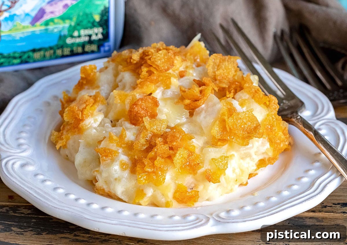 Homestyle Cheesy Potato Casserole 9 A white plate with a generous serving of cheesy potatoes, showing the melted cheese and crunchy topping, with a box of Challenge Dairy butter in the background.