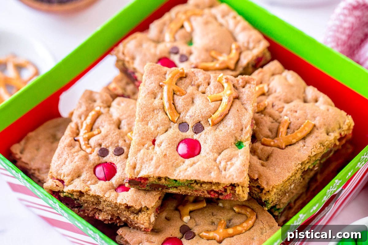 Reindeer Cookie Bars decorated with pretzel antlers, M&M noses, and mini chocolate chip eyes, nestled in a Christmas box.