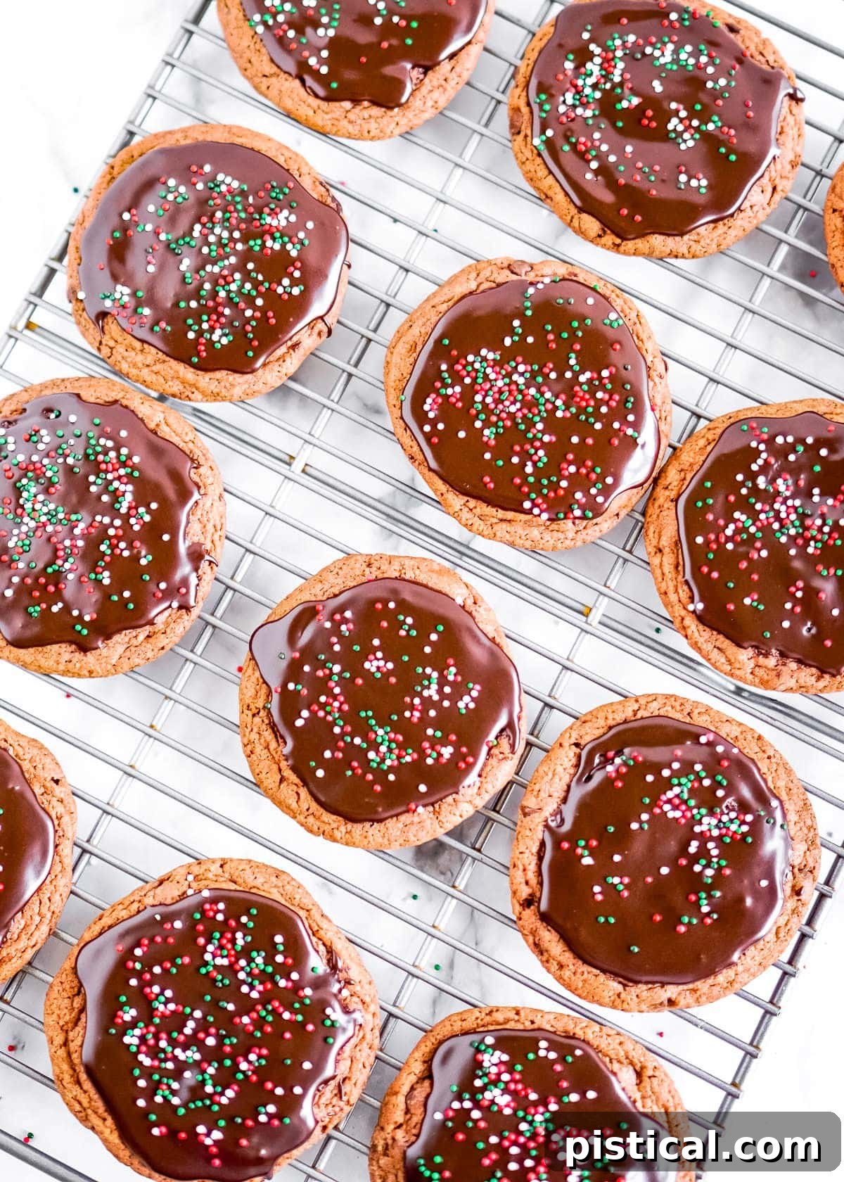 A top-down view of freshly baked chocolate cookies resting on a cooling rack, some already glazed