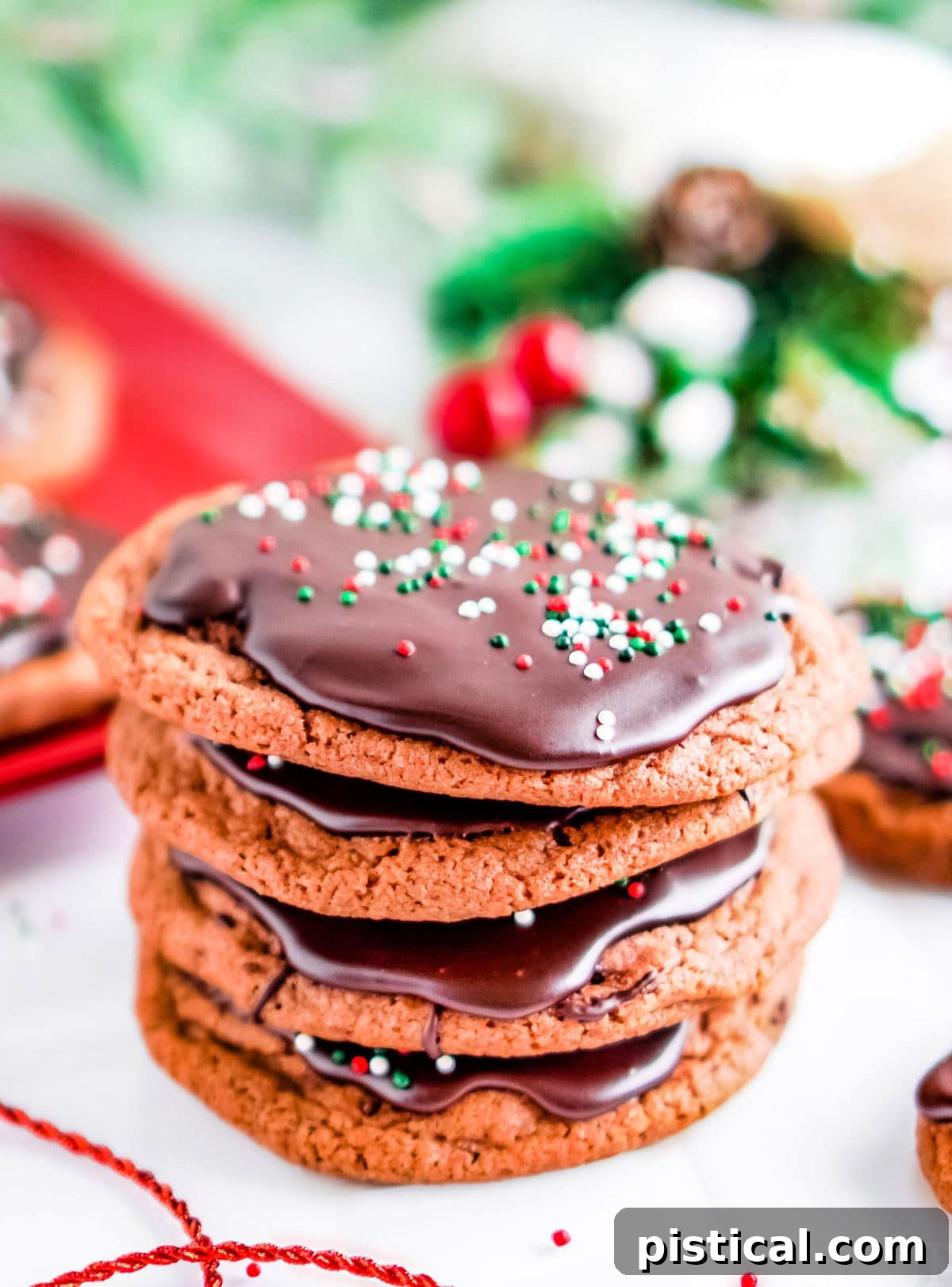 A stack of four chocolate cookies, perfectly glazed and decorated with red, green, and white sprinkles, with festive background decor
