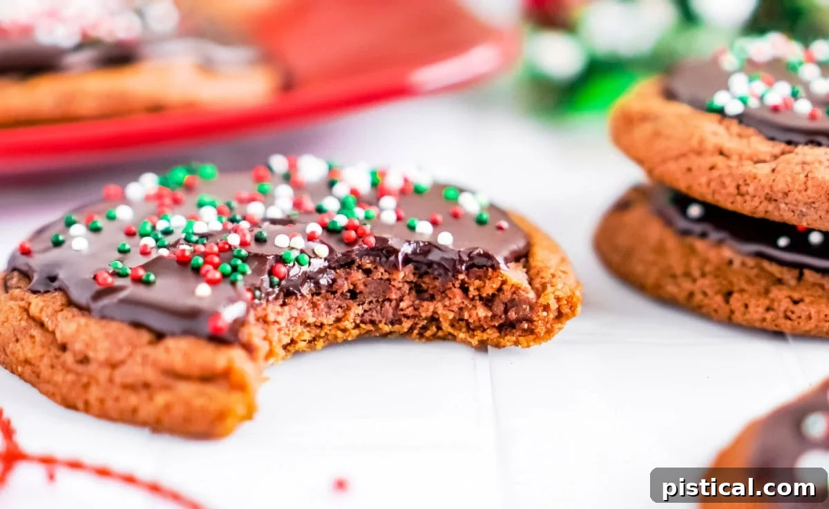 A chocolate cookie with a bite taken out, sitting on a white surface with more glazed chocolate cookies blurred in the background