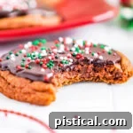 A chocolate cookie with a bite taken out, sitting on a white surface with more glazed chocolate cookies blurred in the background