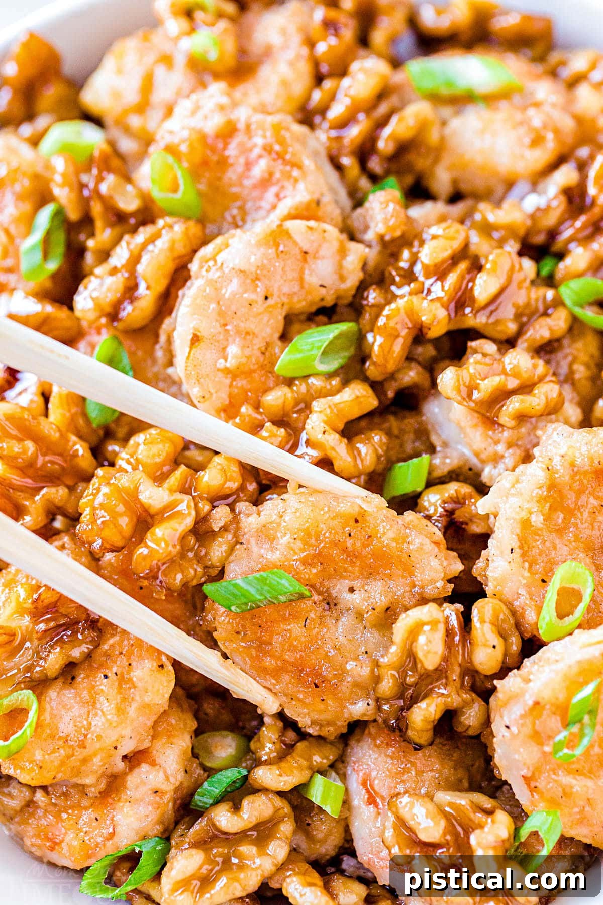 Sweet & Savory Walnut Shrimp Delight 4 A close-up view of a pair of chopsticks holding a piece of Honey Walnut Shrimp, showcasing its crispy coating and the rich sauce, set against the blurred background of the full dish.