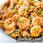 A close-up view of Honey Walnut Shrimp served in a white bowl, elegantly garnished with fresh green onions.
