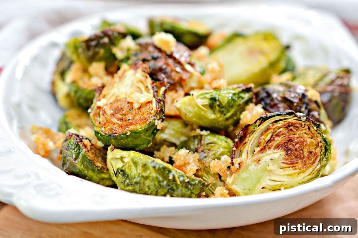 Addictive Air Fryer Brussels with Garlic and Parmesan 3 Close-up of golden brown air fried brussels sprouts in a white bowl, garnished with Parmesan and garlic