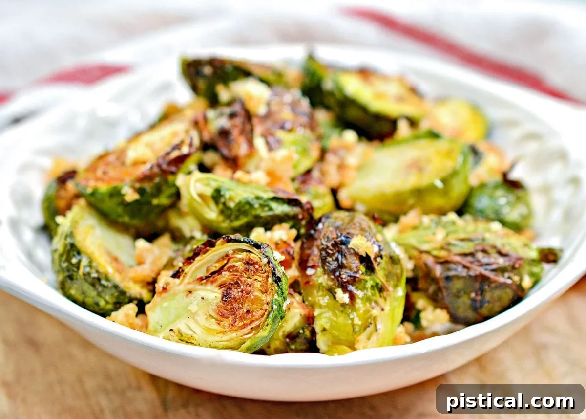 Addictive Air Fryer Brussels with Garlic and Parmesan 6 A white shallow bowl filled with garlic parmesan air fryer brussels sprouts, with a red and white towel in the background