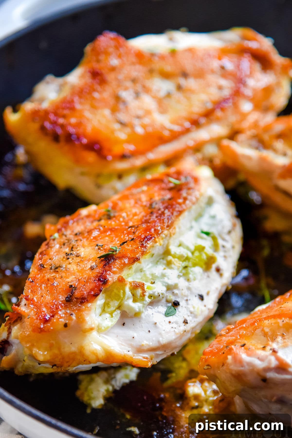 Four golden-brown chicken breasts in a cast iron skillet, brimming with creamy goat cheese filling