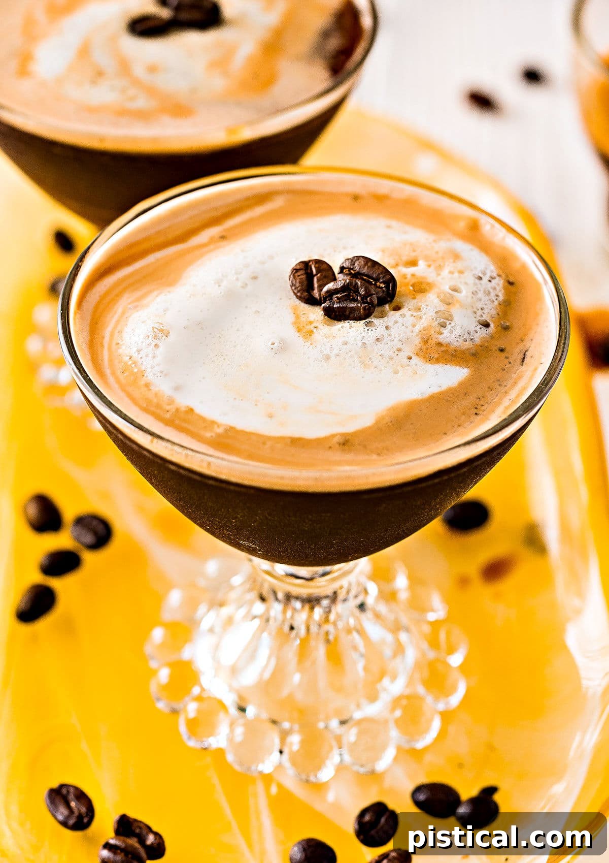 Two perfectly crafted Espresso Martinis, garnished with three coffee beans each, elegantly displayed on a yellow glass tray, seen from a top-down perspective, highlighting their beautiful crema.