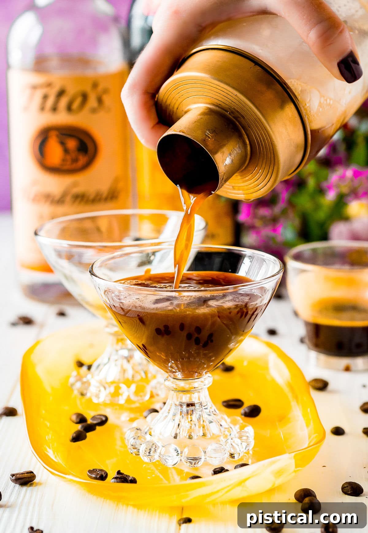 A golden-rimmed cocktail shaker gracefully pours a stream of dark, foamy Espresso Martini into a elegant martini glass, showcasing the cocktail's rich color and texture against a warm background.
