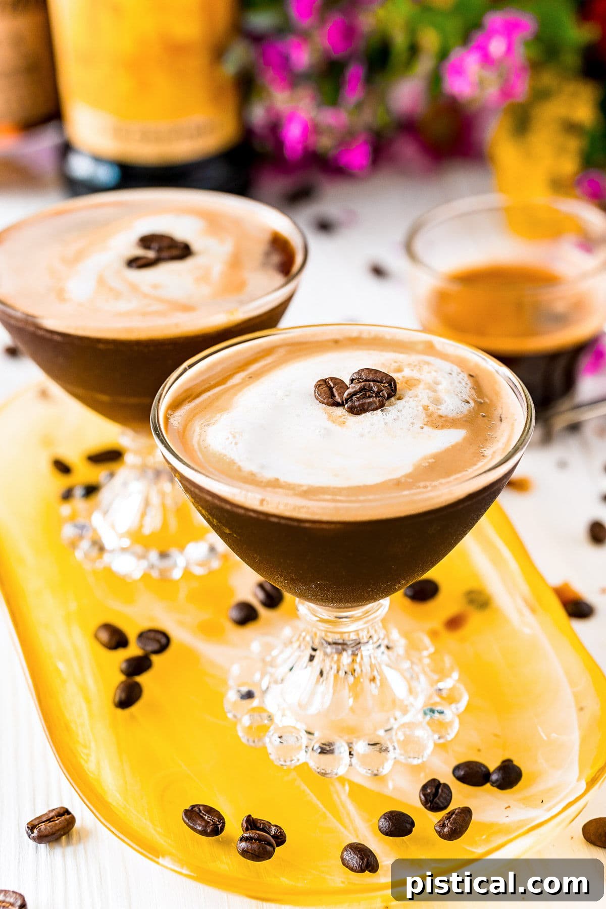Two Espresso Martinis garnished with coffee beans, arranged artfully on a yellow glass tray, with scattered coffee beans around them, evoking a sense of elegance and inviting indulgence.