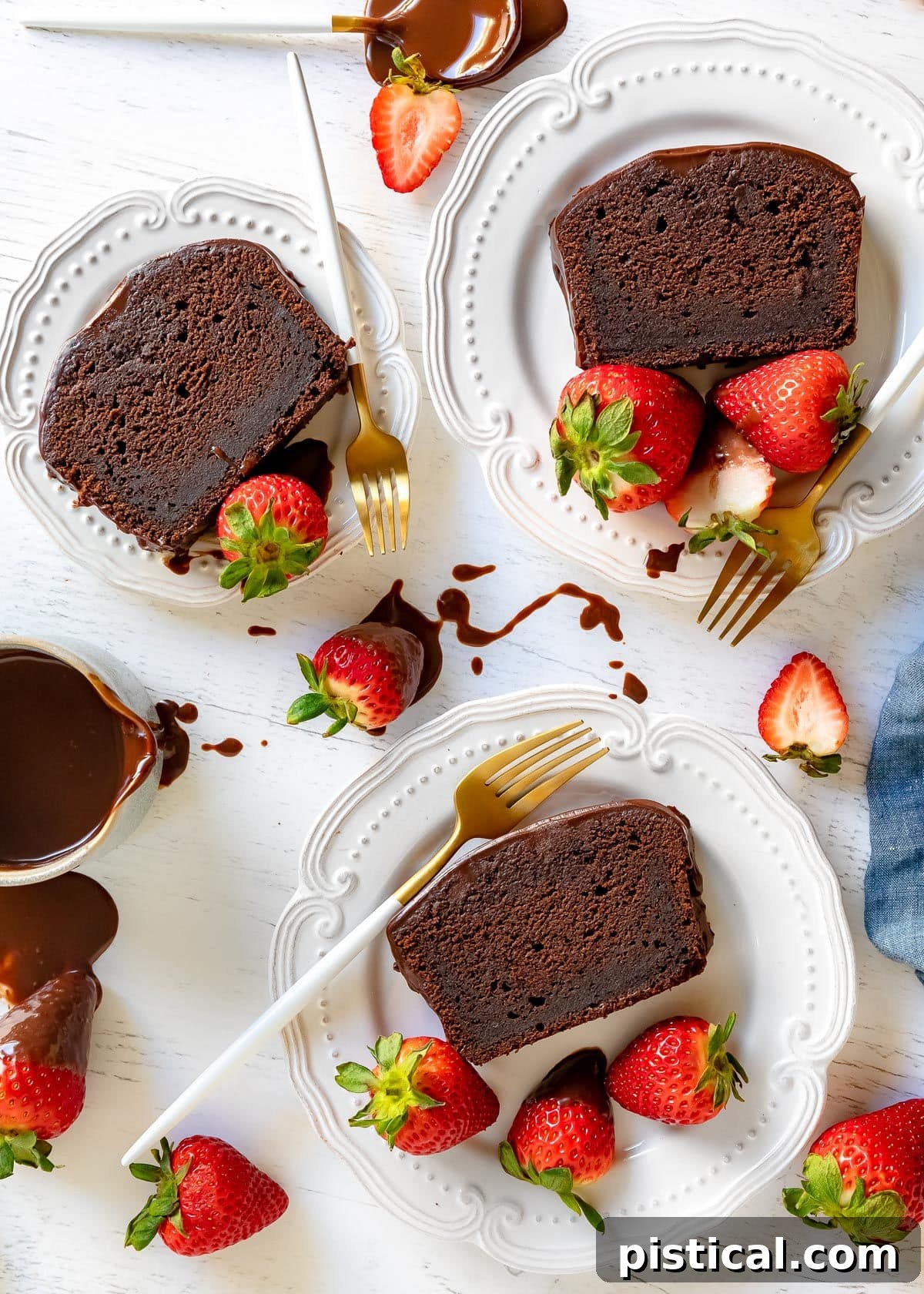 Decadent Chocolate Loaf 10 A top-down composition featuring three perfectly sliced portions of chocolate pound cake on elegant white plates. Each slice is garnished with fresh strawberries, and accompanied by white and gold forks, creating an inviting and luxurious dessert presentation.