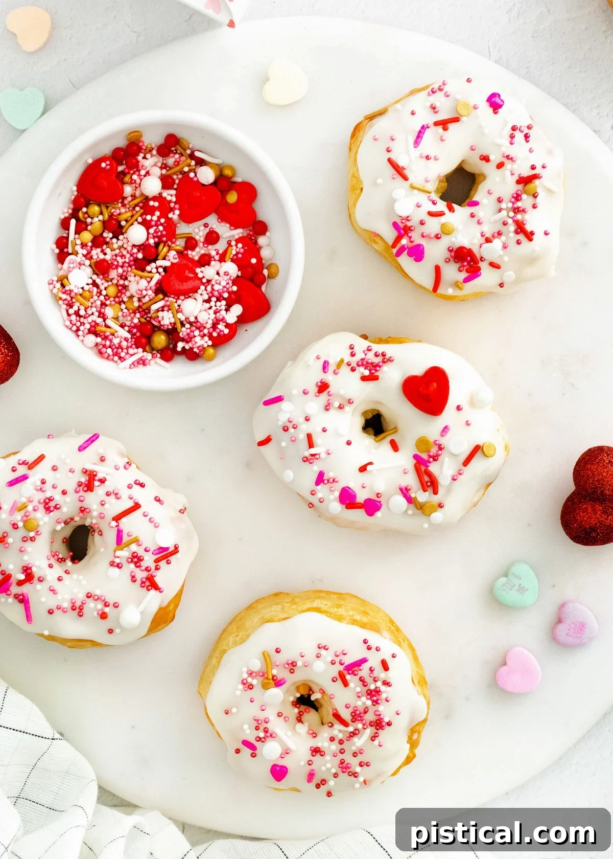 Easy Air Fryer Biscuit Donuts 4 Four air fryer donuts, festive with Valentine's Day decorations, artfully arranged on a round marble surface.