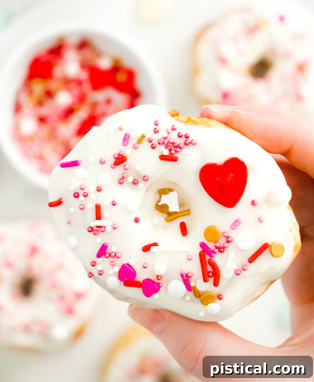 Easy Air Fryer Biscuit Donuts 5 A beautifully decorated air fryer donut being held aloft, with a tray of other glazed donuts visible below.