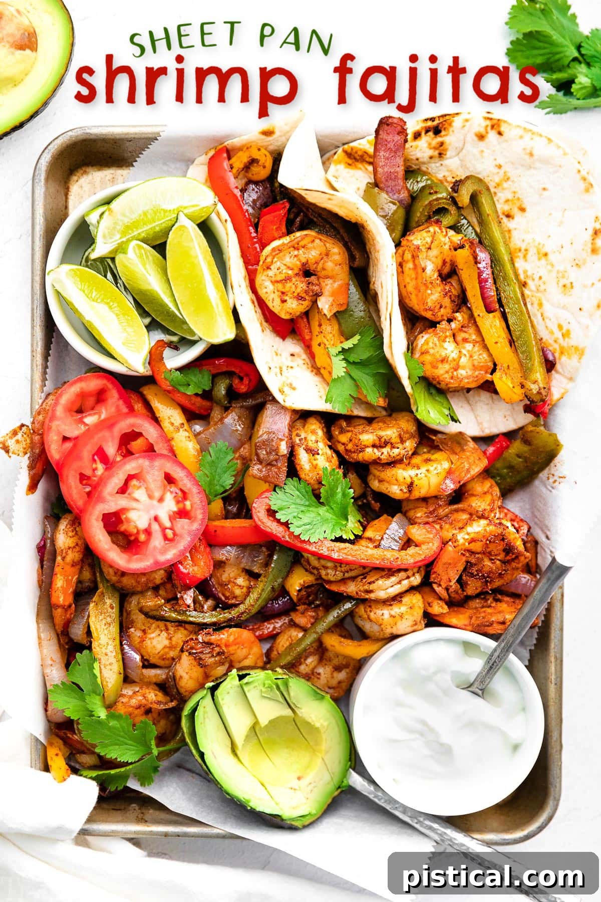 Sizzling Sheet Pan Shrimp Fajitas 2 shrimp fajitas on a sheet pan with all the fixings including avocado lime wedges and sour cream.