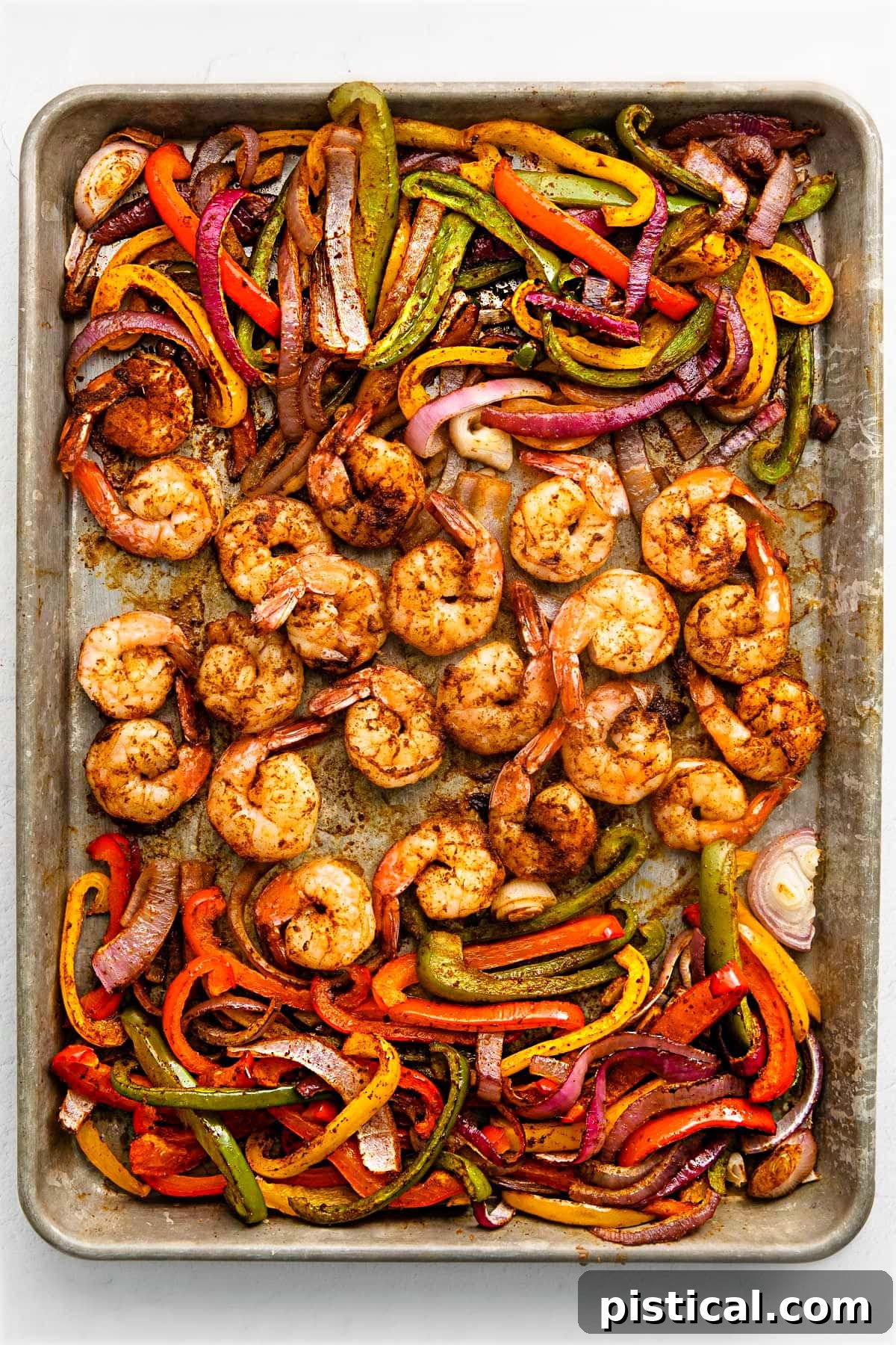 Sizzling Sheet Pan Shrimp Fajitas 7 shrimp fajitas on a sheet pan with shrimp in the center and veggies on the sides.