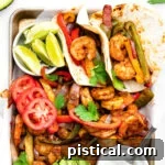 shrimp fajitas on a sheet pan with all the fixings including avocado lime wedges tomatoes and sour cream.
