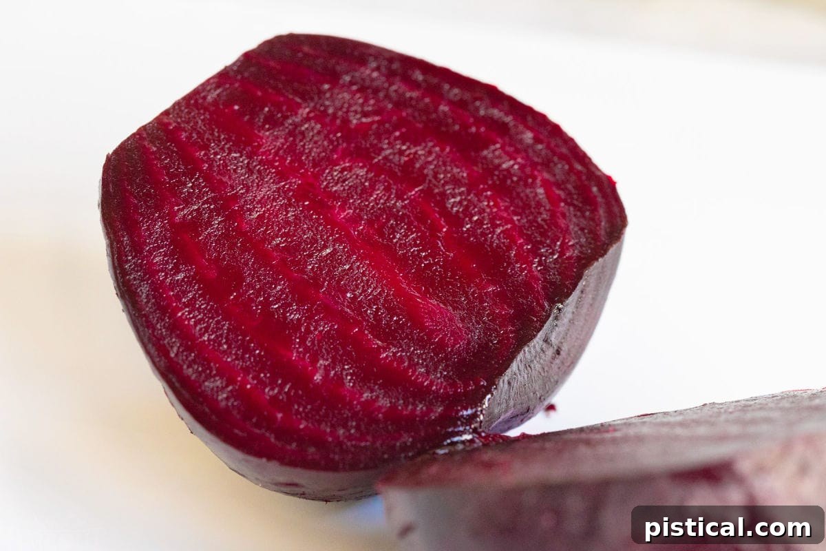 How to Make Perfect Roasted Beets 3 A vibrant red roasted beet, perfectly cut in half on a white cutting board, showcasing its tender texture.