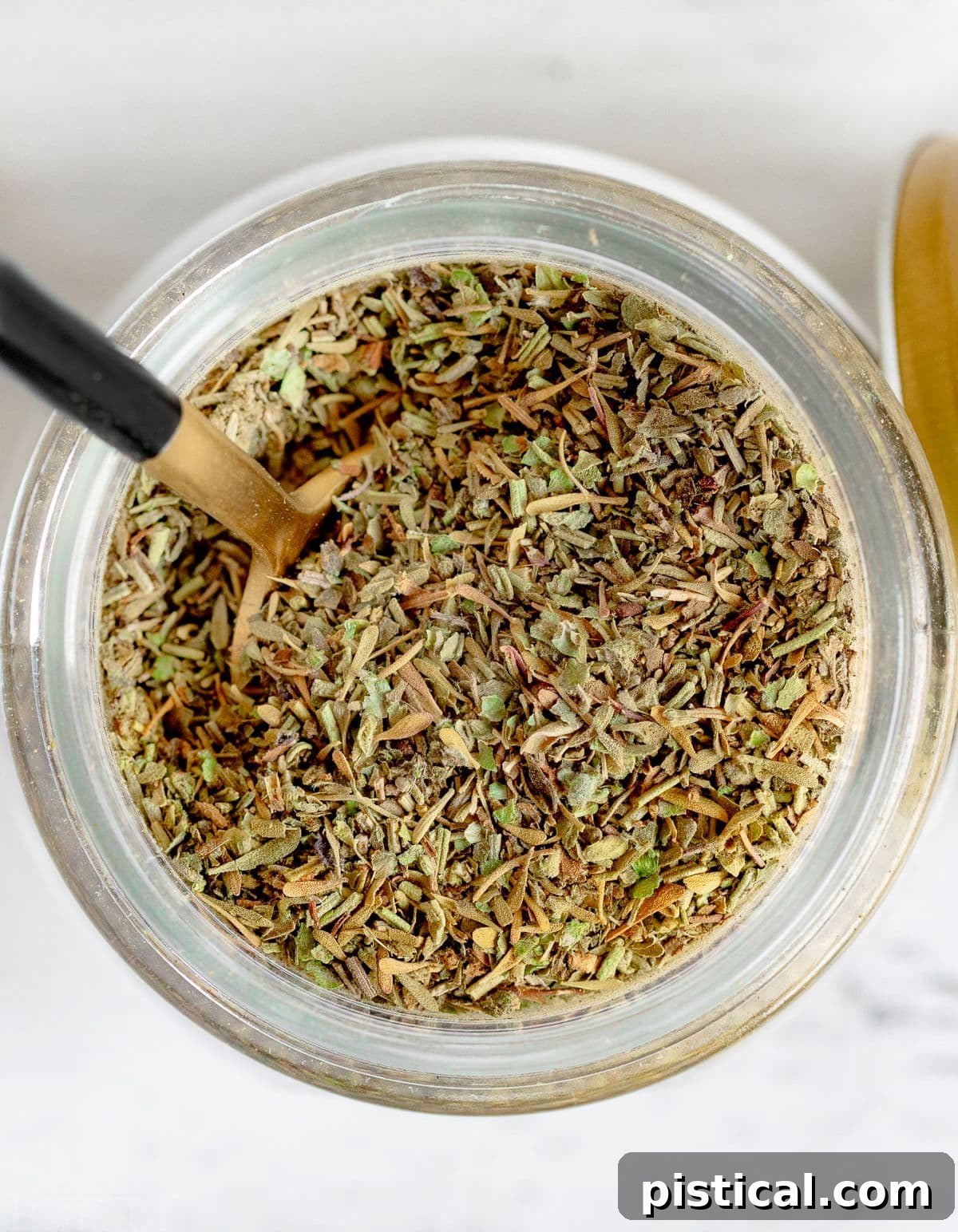 Top-down view of a glass jar filled with mixed Italian seasoning herbs.