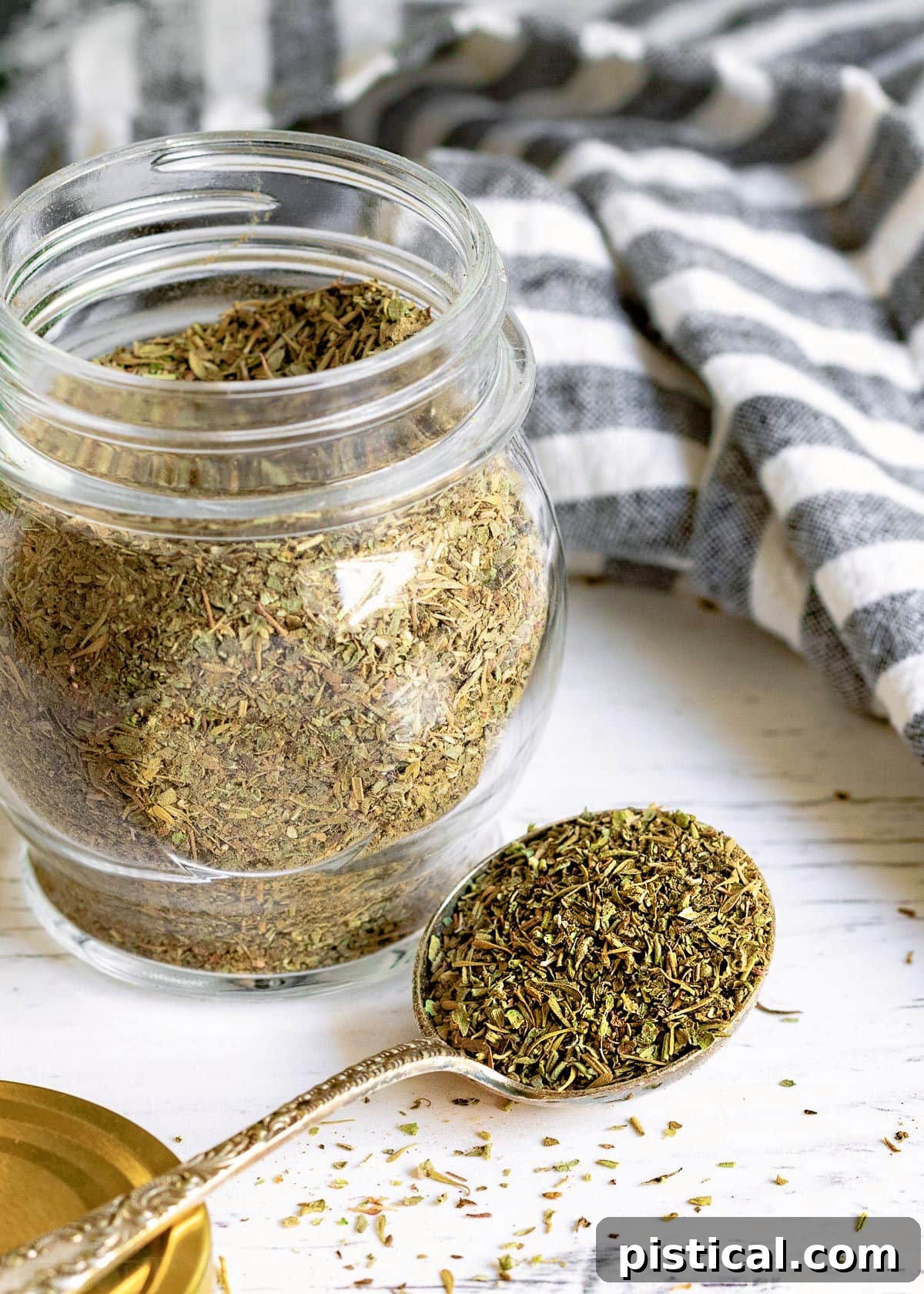 A spoonful of Italian seasoning mix held in front of a glass jar.