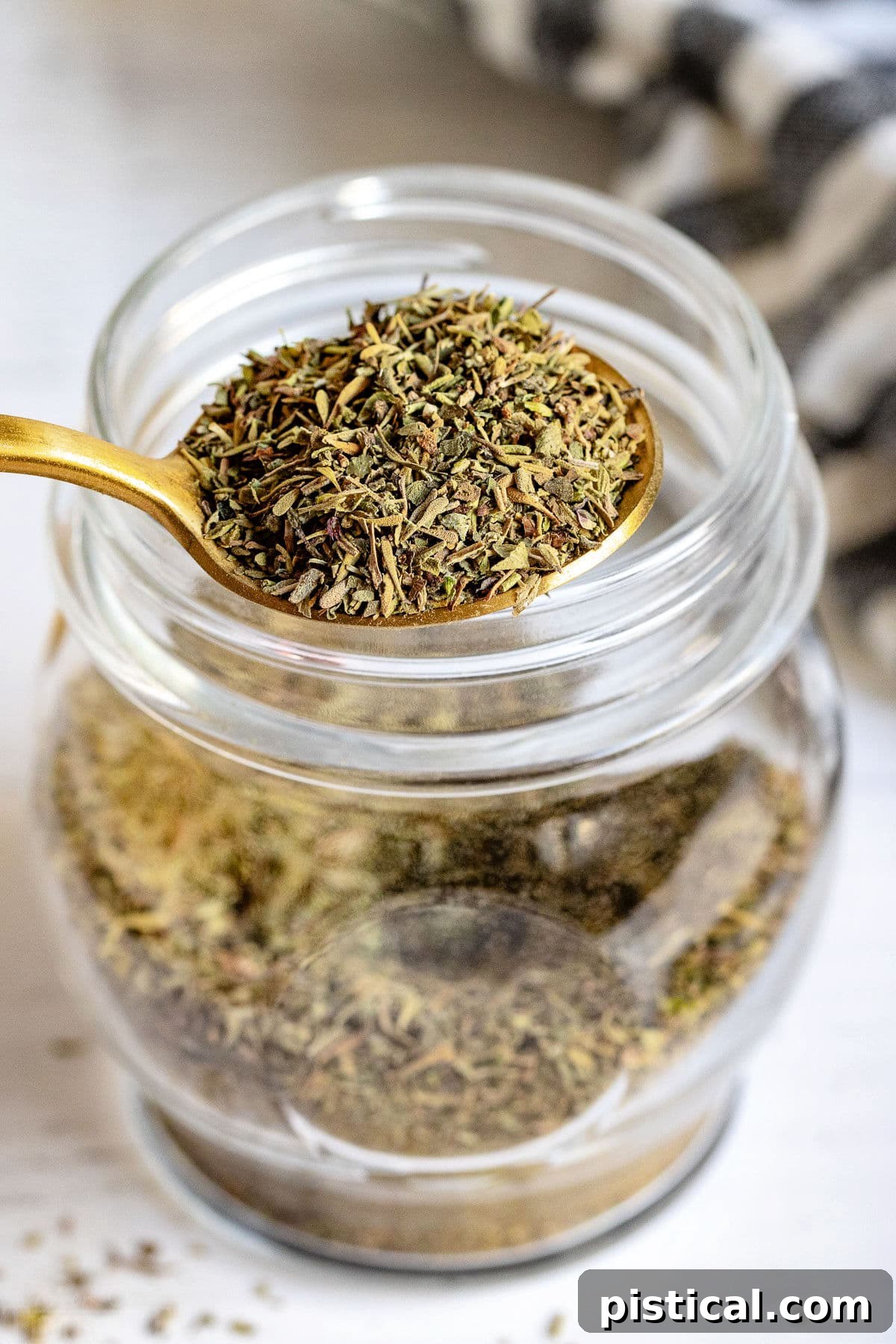 A spoonful of Italian seasoning held above a jar, illustrating its fresh, vibrant texture.