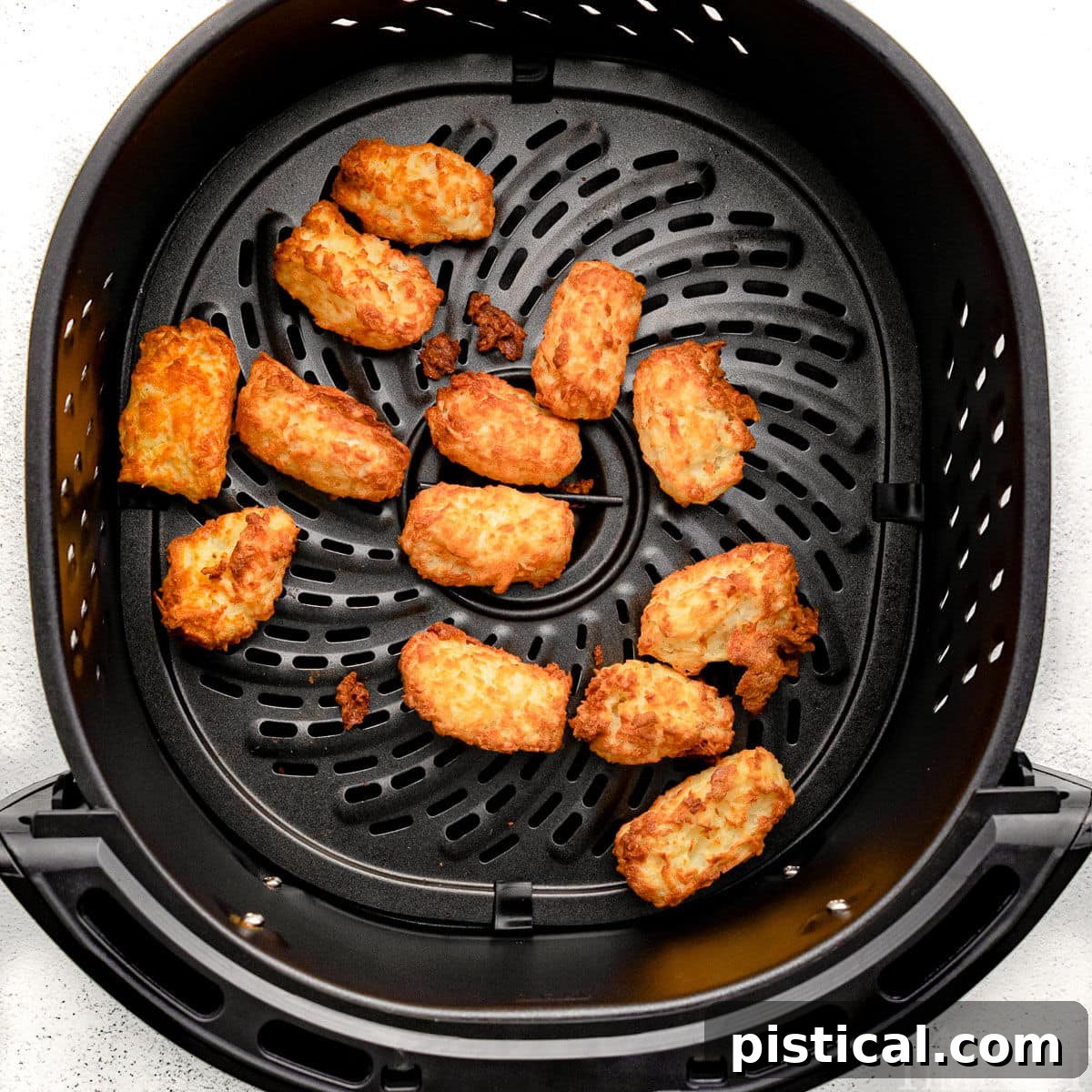 Freshly cooked, golden and crispy tater tots resting in an air fryer basket, steam gently rising.
