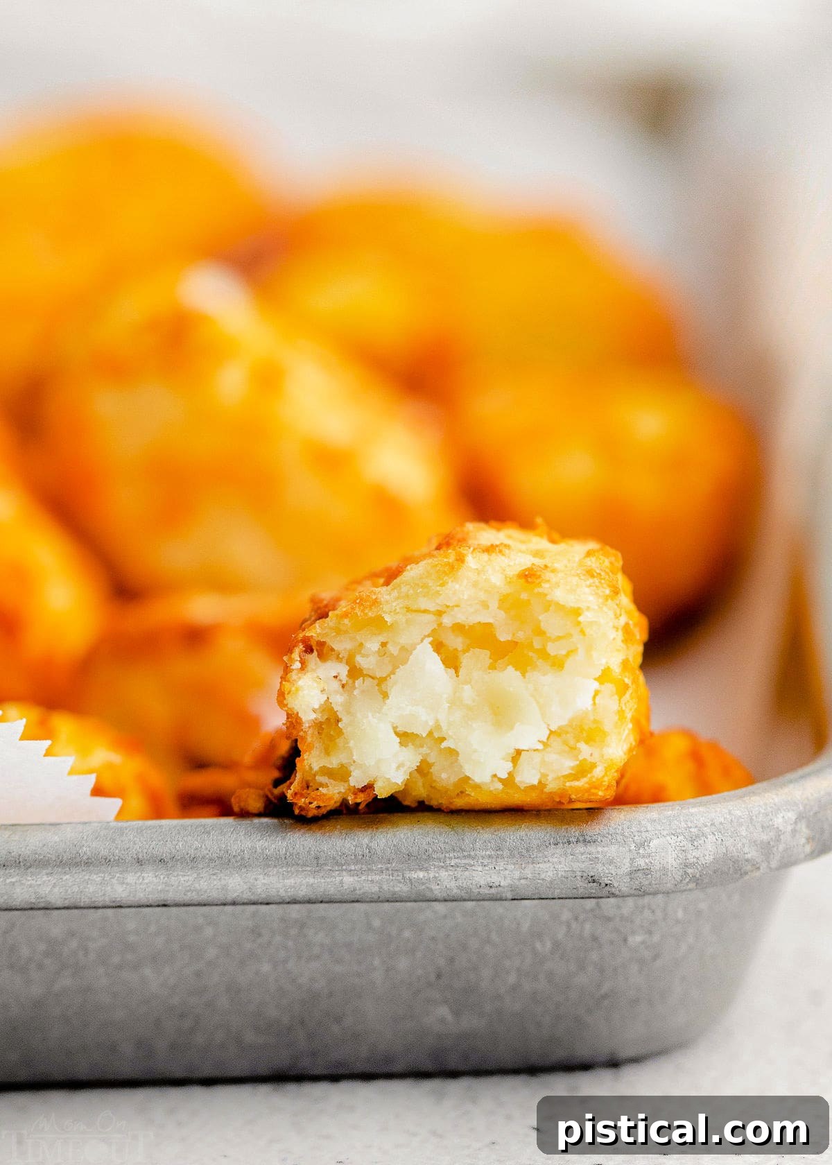 A tater tot cut in half, revealing its fluffy potato interior and crispy exterior, with a small bowl of ketchup in the background.