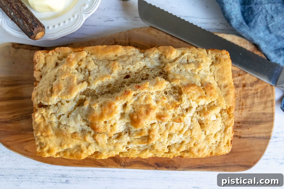 A freshly baked loaf of beer bread resting on an olive wood cutting board, with a bread knife beside it, ready for slicing.