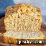 A slice of beer bread on a board next to a whole loaf.