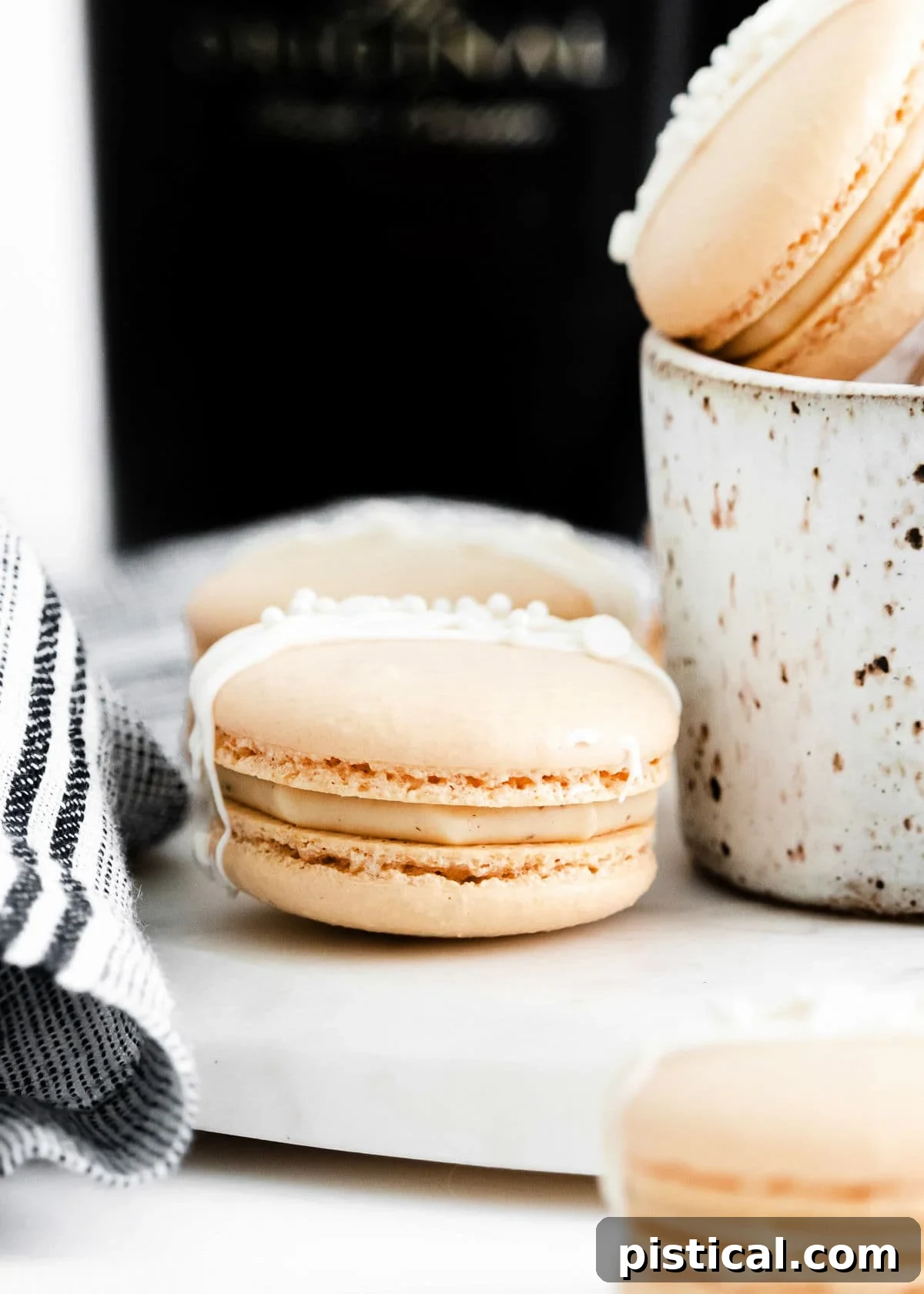 Baileys Macarons 4 Close-up view of two beautifully drizzled Irish cream macarons, showcasing their perfectly formed feet and smooth tops.