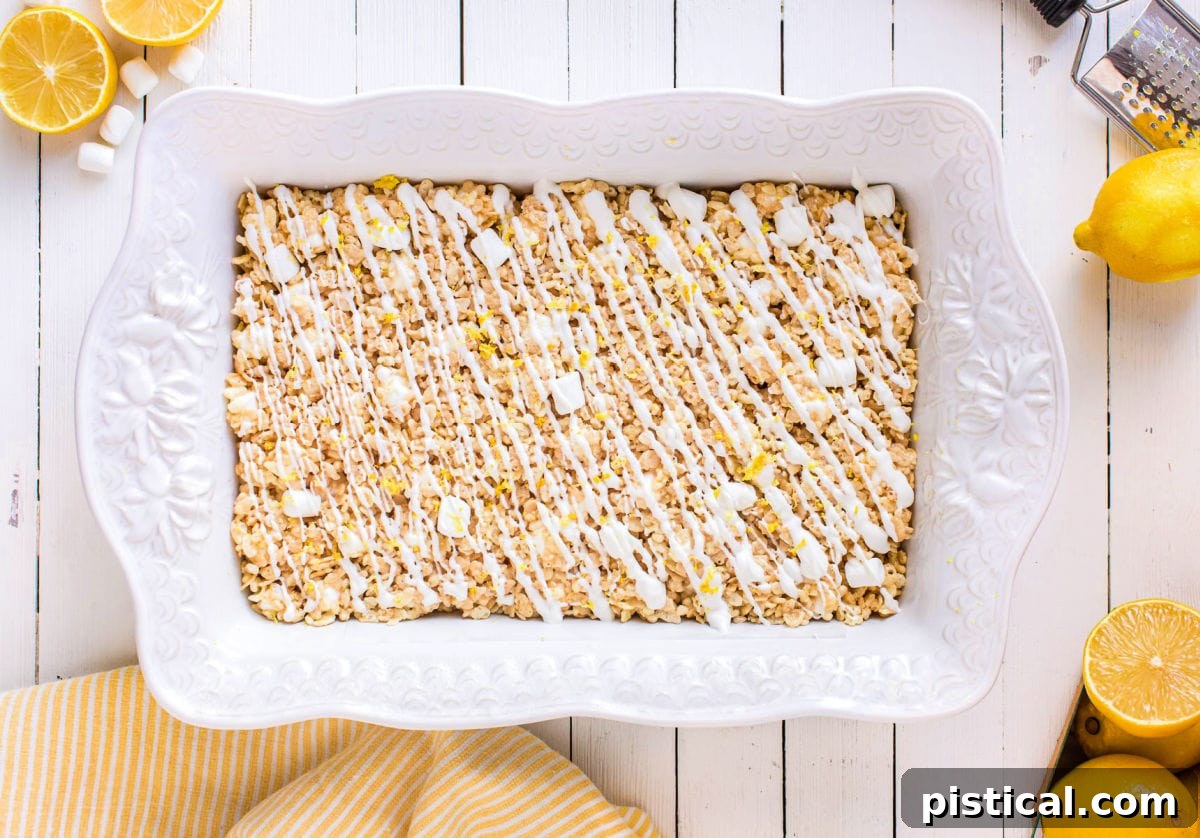 Zesty Lemon Krispie Squares 5 Freshly prepared lemon rice krispie treats cooling in a white baking dish, ready to be sliced and served.