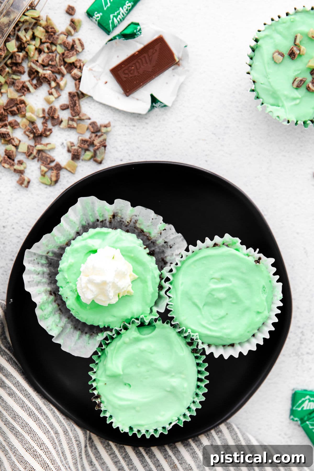 A top-down view of vibrant green mini cheesecakes, some topped with a swirl of whipped cream, resting on a sophisticated black plate, ready to be enjoyed.